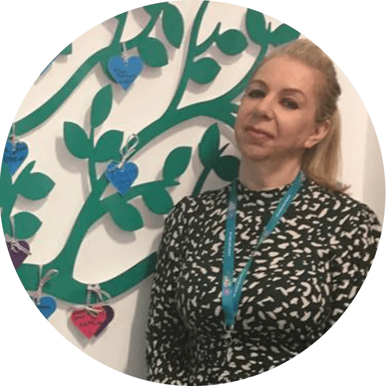 Amanda has blonde hair and is wearing a black dress, stood in front of the chsf donation tree