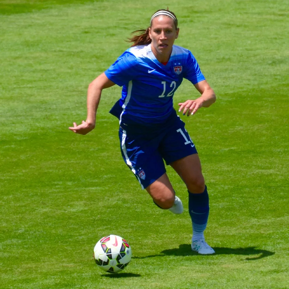 Lauren playing football. She is on the pitch in an all blue kit. She is running.