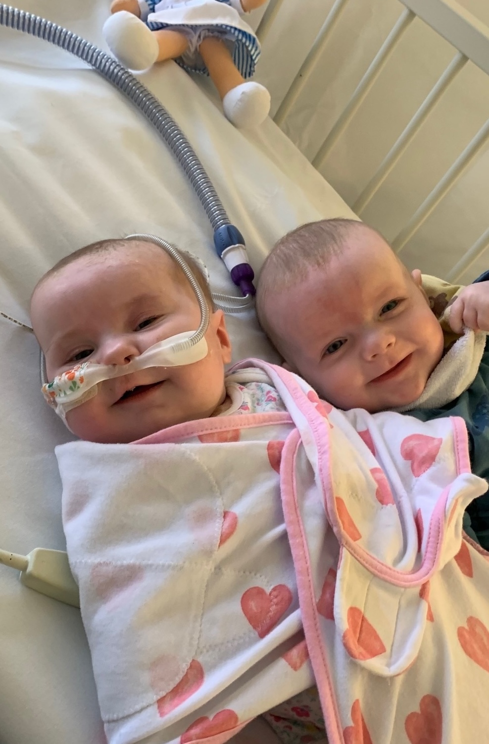 Roxy laying in a hospital bed smiling with her twin brother