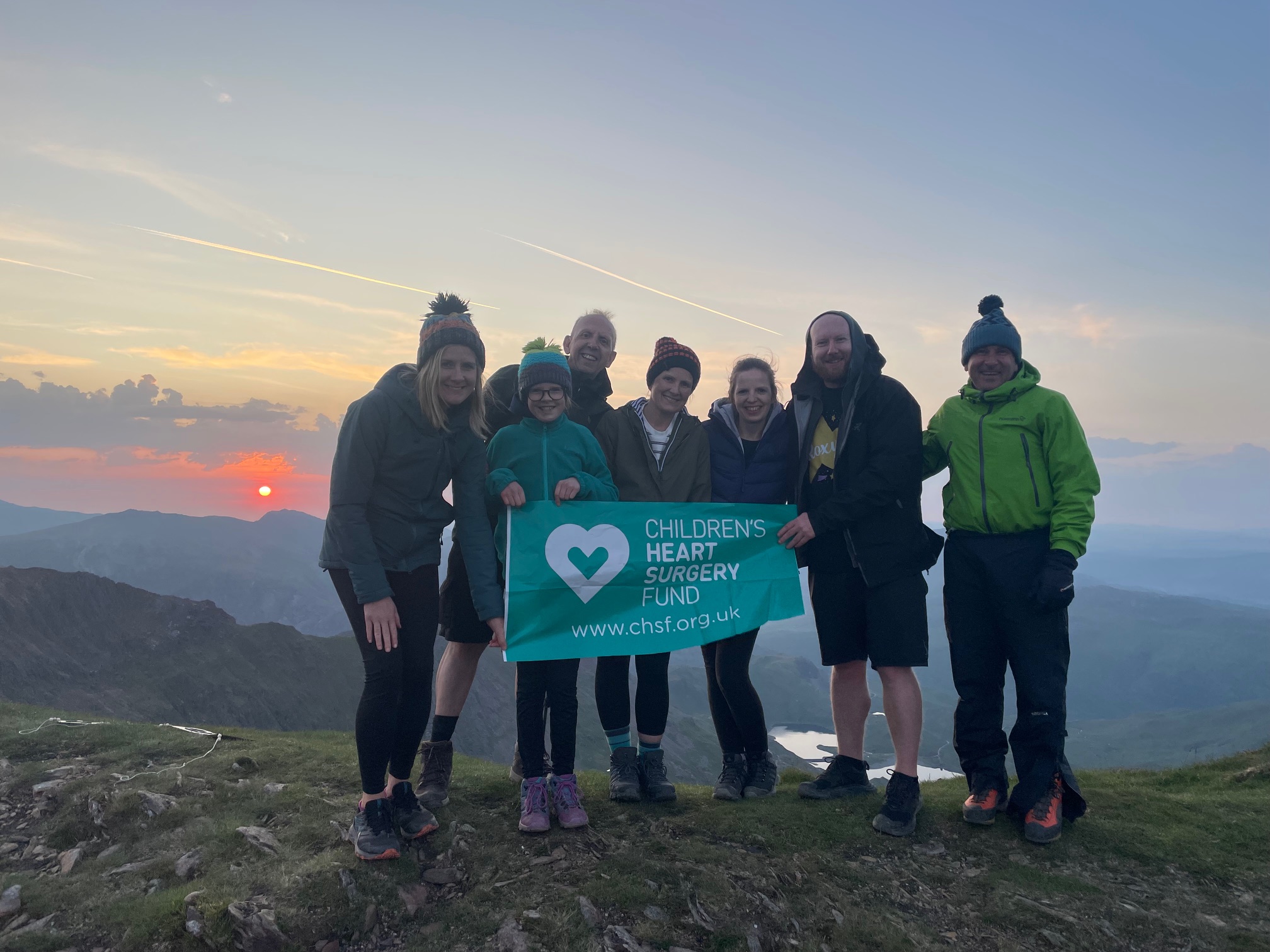 The Jackson Family at sunrise on top of Snowdon, holding a green CHSF banner