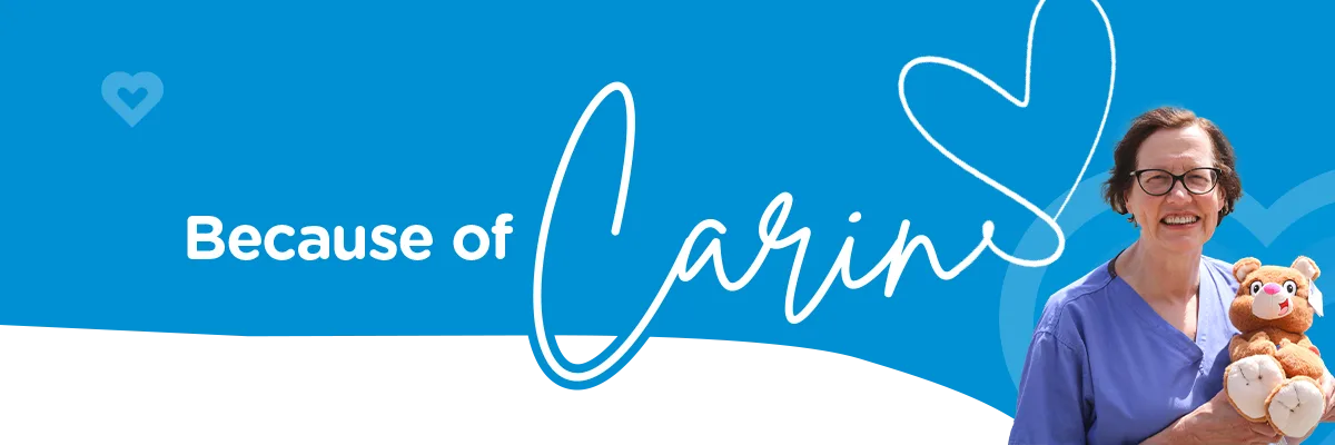 Blue banner with hearts that reads 'Because of Carin' Carin is in cursive with a heart drawn at the end of the 'n'. Photo of Carin Van Doorn smiling and holding a Katie Bear