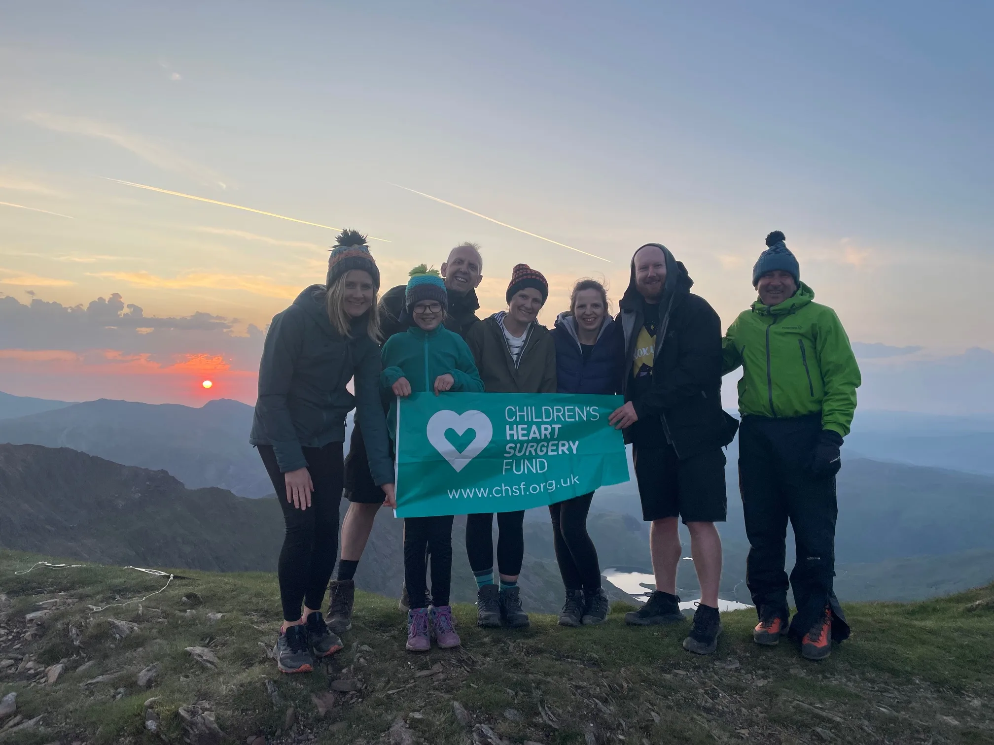 The Jackson Family at sunrise on top of Snowdon, holding a green CHSF banner