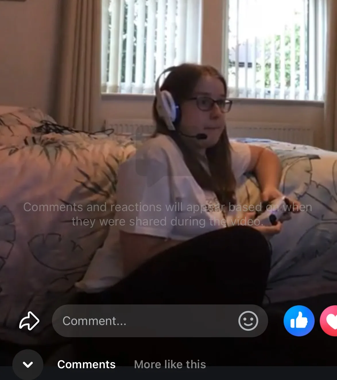 jessica wearing a white CHSF tshirt and gaming headphones, sat on th efloor of her bedroom holding a playstation controller. The image is a screengrab from a Facebook live