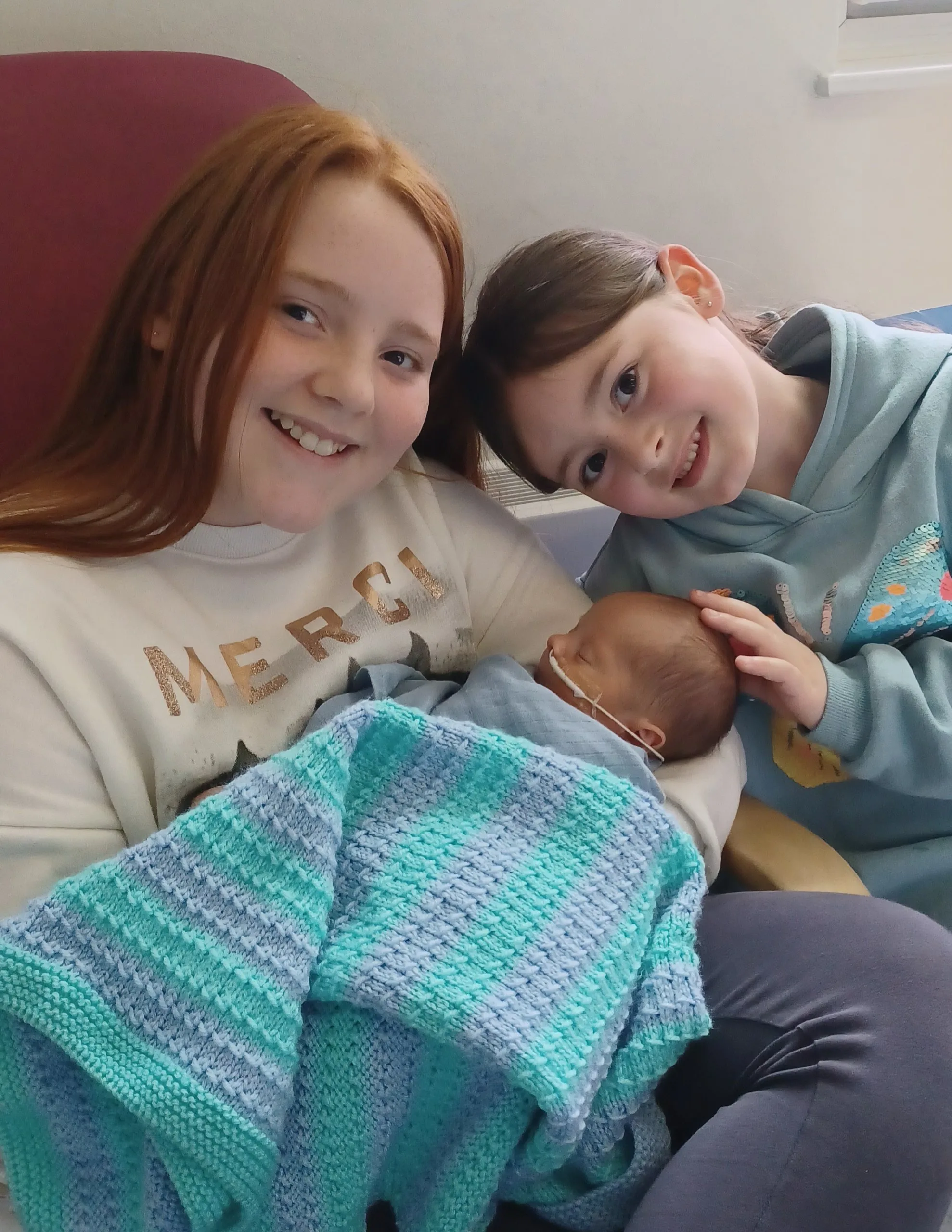 Lochie being held as a baby by his two sisters