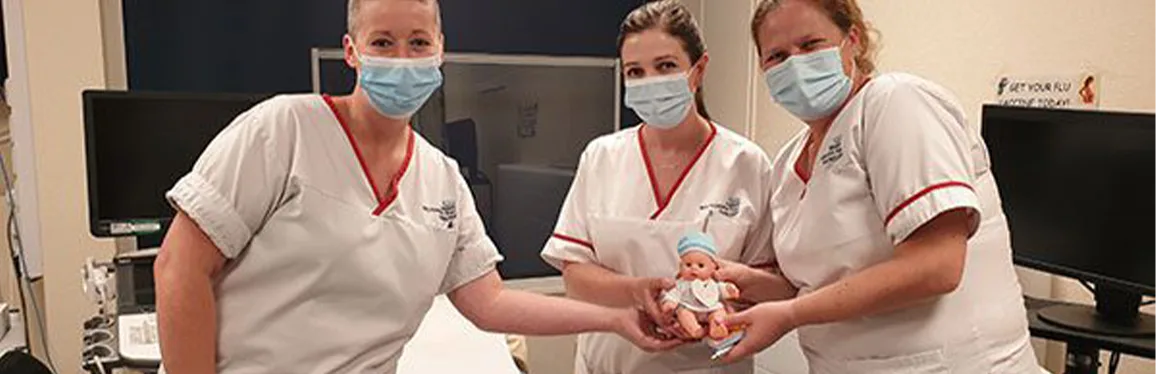 Three nurses in scrubs and masks holding a doll