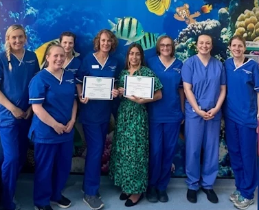 Echo team wearing blue scrubs, standing in a line, smiling, holding their certificate for the accreditation