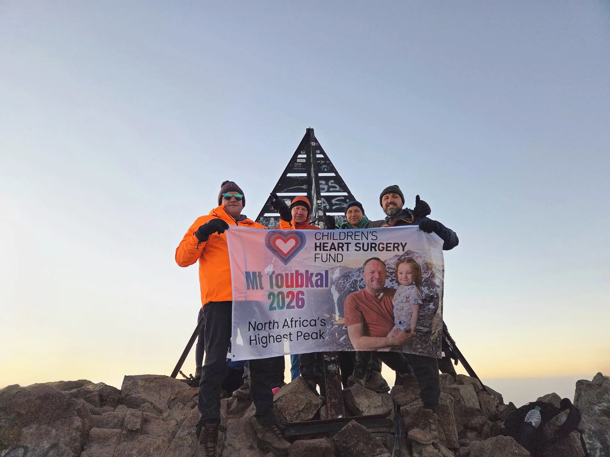 The group at Mount Toubkal summit with CHSF banner. It is sunrise.