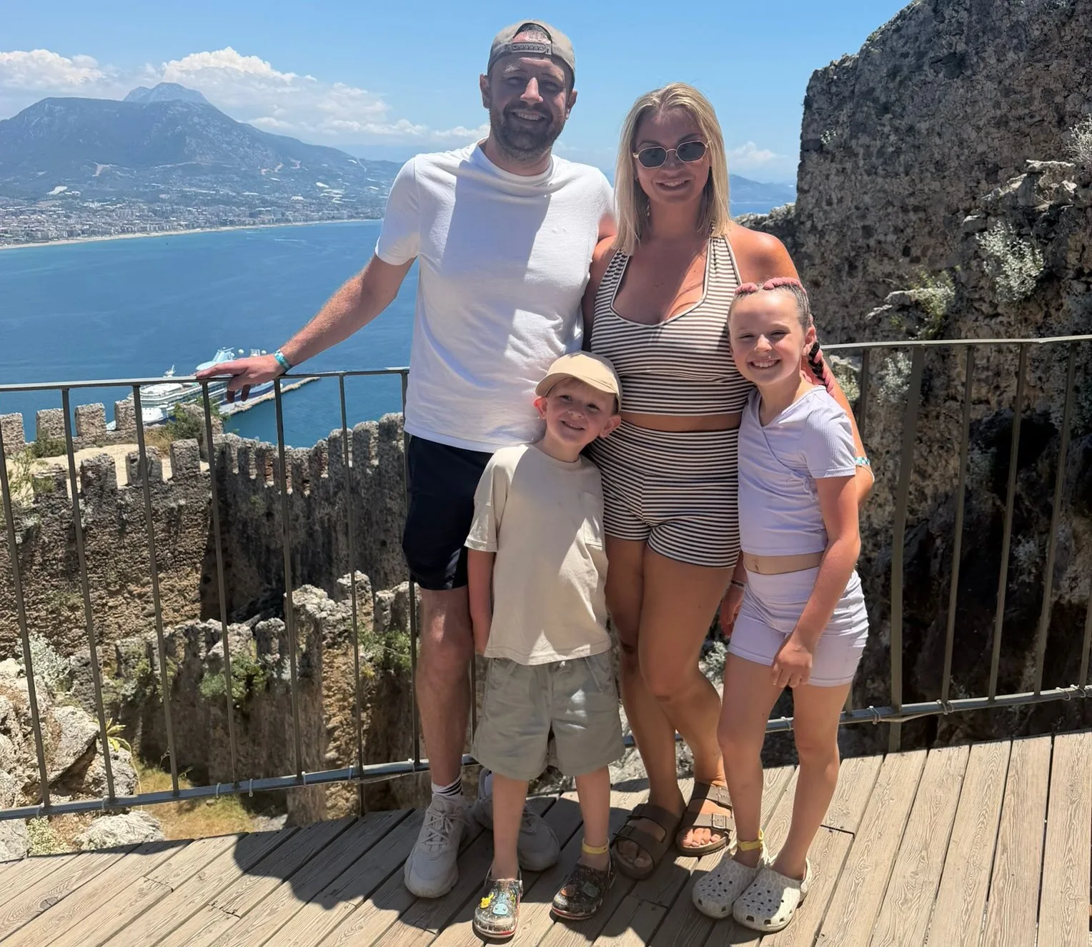 Steven with his wife and two children in front of a scenic background. There is a mountain and sea behind them.